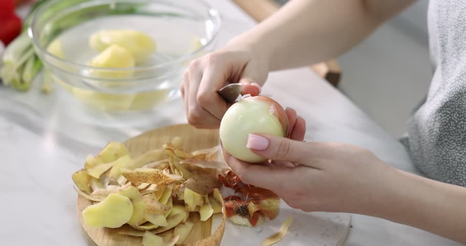 Woman peeling fresh onion at white table indoors, closeup. Camera moving forward