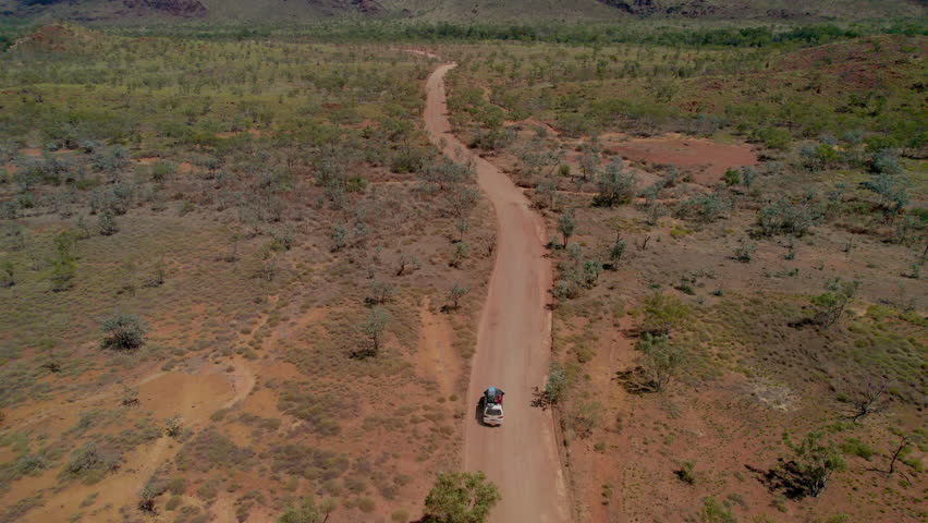 Aerial drone shot following a 4WD vehicle driving along a remote dirt road leaving the Bungle Bungles in Purnululu National Park, Western Australia. Rugged outback landscape, adventure travel and remo