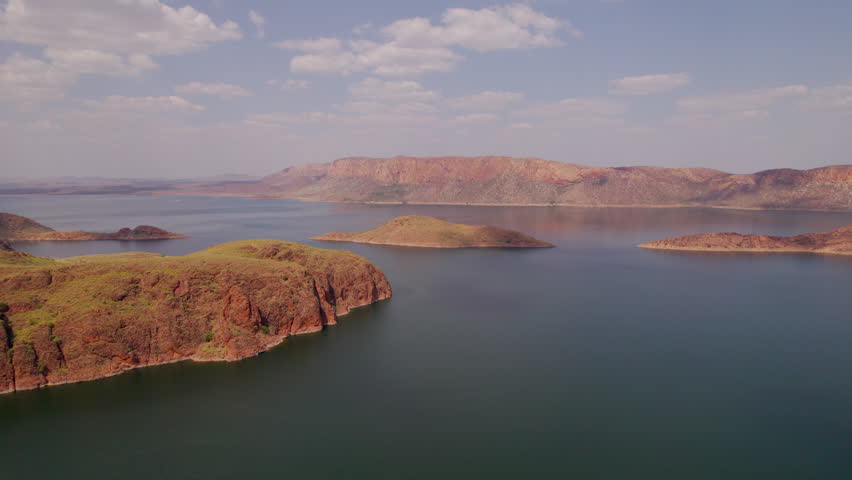 Drone flying forward and descending over the turquoise waters of Lake Argyle in Western Australia, revealing rugged islands and vast remote Kimberley landscape under soft daylight.