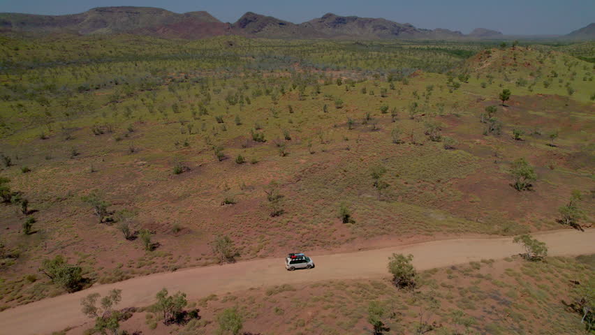 Aerial drone shot following a 4WD vehicle driving along a remote dirt road leaving the Bungle Bungles in Purnululu National Park, Western Australia. Rugged outback landscape, adventure travel