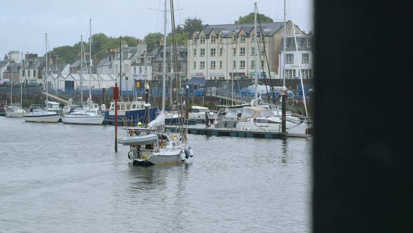 A yacht sails into Stornoway harbour. Anchored boats line the pontoon.