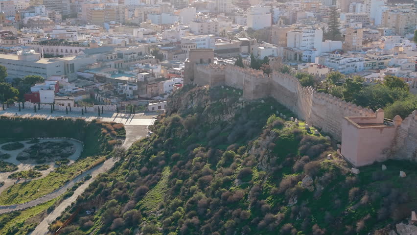 Sunlight illuminating the ancient walls of the Alcazaba of Almeria. This aerial shot reveals the historic fortress and its gardens overlooking the city