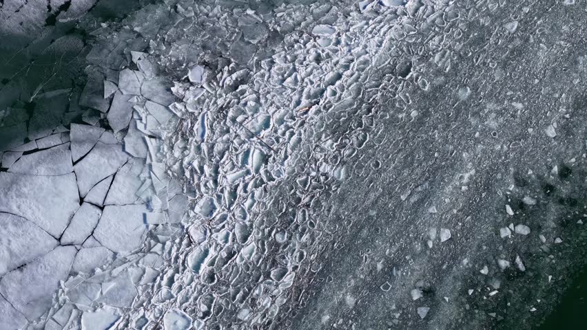 Aerial top down drone view of broken ice floes along the edge of a frozen river or lake during winter in Montana
