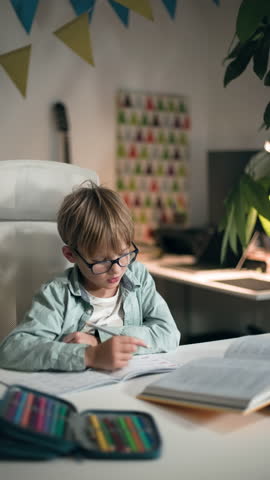 A child wearing glasses yawns while sitting at a table and doing homework