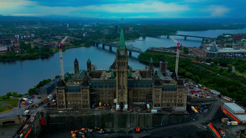 Parliament Hill from an aerial perspective during renovations at the front entrance on a summer twilight day in the foreground and the background showing the river and a bridge to bordering Quebec