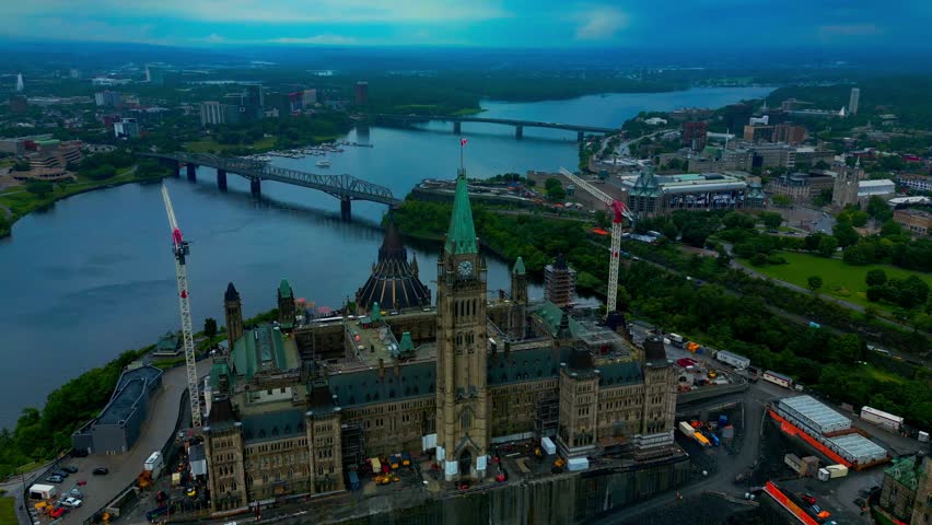 Parliament Hill in Ottawa offers a birds eye aerial view 180 degree flight of construction cranes by the area and surrounding property on a summer day with lush green foliage stunning horizon view