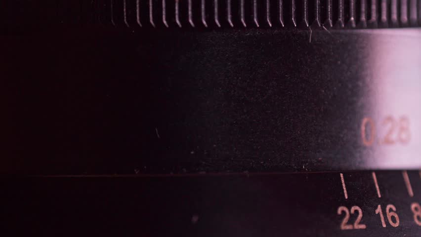 Extreme macro footage of a hand rotating the aperture ring on a classic manual camera lens with visible scale markings.