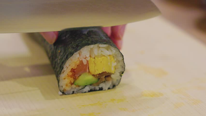 Close-up of hands cutting futomaki sushi roll with a kitchen knife