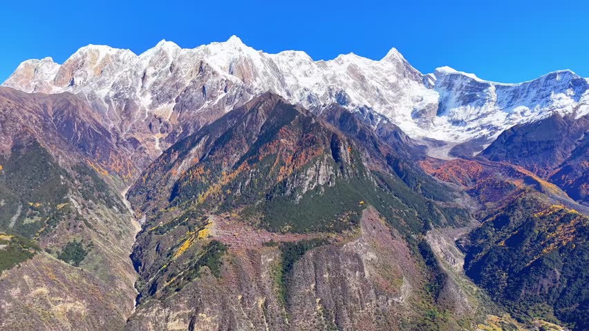 Aerial view of snow-capped mountain peaks with forested valleys and clear blue sky
