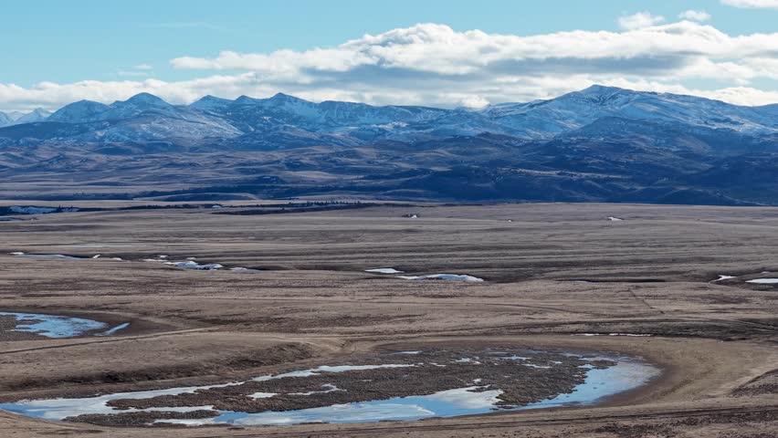 Aerial view of a wide open plain with meandering river channels and fields against the backdrop of the snow-capped Rocky Mountains near Whitefish, Montana.