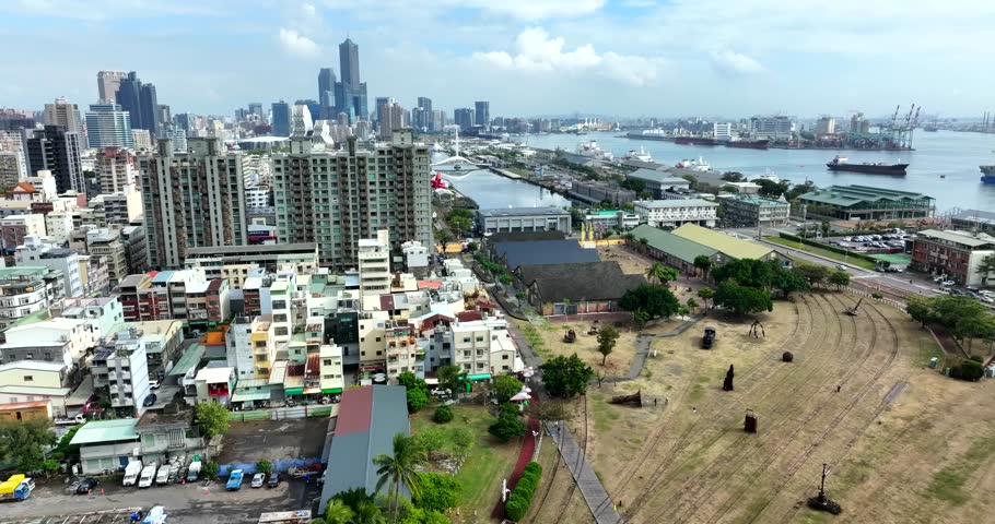 Establishing aerial shot of Kaohsiung, Taiwan, showing dense urban development with residential and commercial towers, layered skyline and harbor infrastructure in distance. Wide shot.