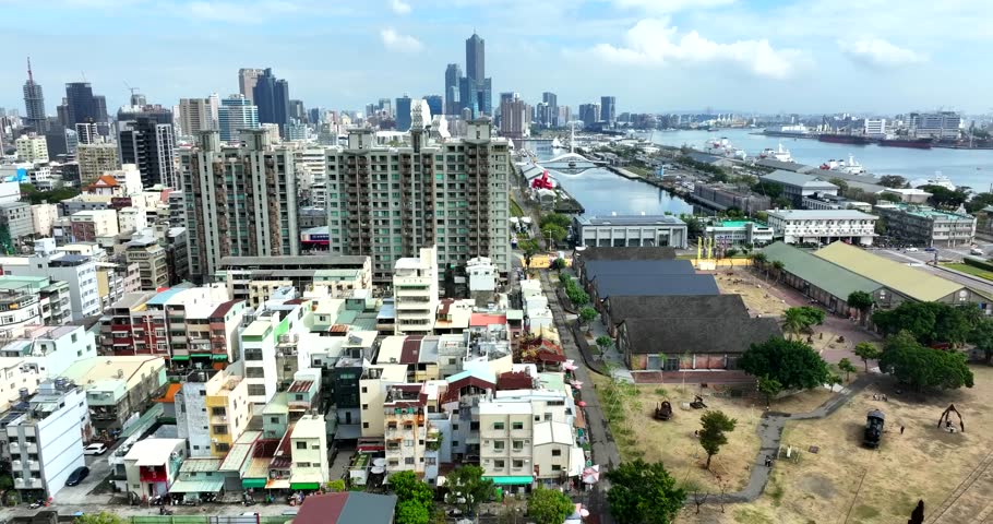 Establishing aerial shot of Kaohsiung, Taiwan, showing dense urban development with residential and commercial towers, layered skyline and harbor infrastructure in distance. Wide shot.