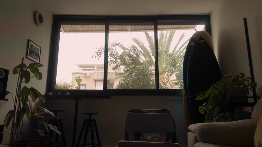 Heavy dust storm timelapse weather outside a residential home window with plants and surfing gear visible.