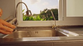 First Person View Of Hand Filling Glass With Tap Water Under Kitchen Faucet Before Measuring Ppm With Digital Tester Near Window With Tropical Green Landscape. Drinking Water Quality Check. - Powered by Shutterstock - Get 15% off with code: PIKWIZARD15