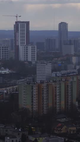 Aerial sweep over Katowice, Poland shows a crane topped high rise, modern office towers, prefabricated blocks, and houses under overcast late afternoon light.