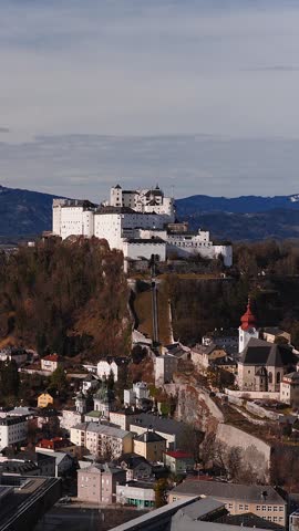Aerial view of Hohensalzburg Fortress in Salzburg, Austria. The old town, red domed church, funicular, and Alpine peaks appear in crisp winter light.