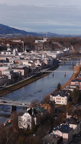 Aerial pan and descent over Salzburg, Austria show the Salzach River, bridges, Hohensalzburg on Festungsberg, Baroque towers, villas, cliffs, cars and people in late autumn.