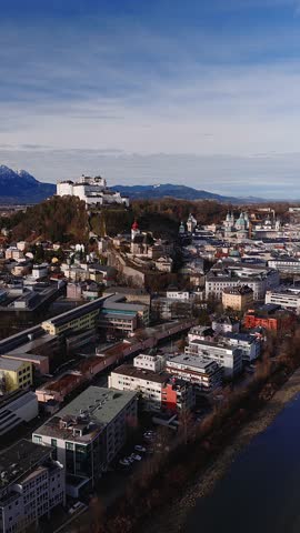 Aerial daylight view of Salzburg, Austria as a drone tracks, showing Salzach River, multiple bridges, Hohensalzburg Fortress, baroque domes, and leafless trees in late autumn.