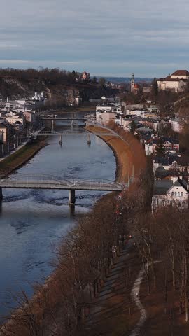 Aerial view of Salzburg, Austria shows the Salzach River, bridges, Salzburg Cathedral domes, and Hohensalzburg Fortress as a slow vertical pan tracks along.