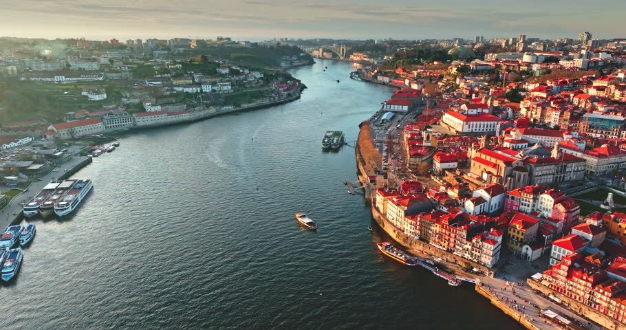 Portugal cityscape aerial view. Porto historic Ribeira district with vivid rooftops along the curving Douro River, with boats docked and navigating the water under the warm glow of late afternoon sun