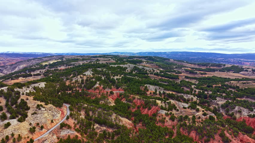 A wide view shows hills and valleys covered in trees. A winding road cuts through the landscape. The sky is cloudy with patches of blue. It is early afternoon in the countryside.
