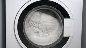 Washing machine drum spinning with clothes. Closeup of a front-loading washing machine with the drum spinning, washing white laundry and linens during a cleaning cycle. Modern household appliance - Powered by Shutterstock - Get 15% off with code: PIKWIZARD15