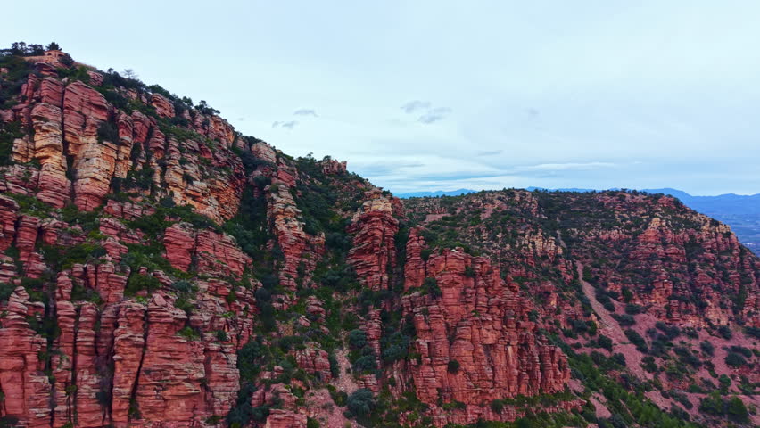 The scene shows rock formations in Sedona, Arizona. The rocky cliffs rise sharply with patches of green below. Clouds are present in the sky adding depth to the view.