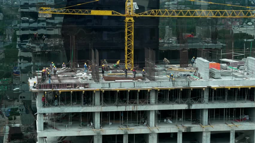 Group of Construction Workers in Safety Gear Working on High-Rise Building Development with Yellow Tower Crane in Urban Cityscape