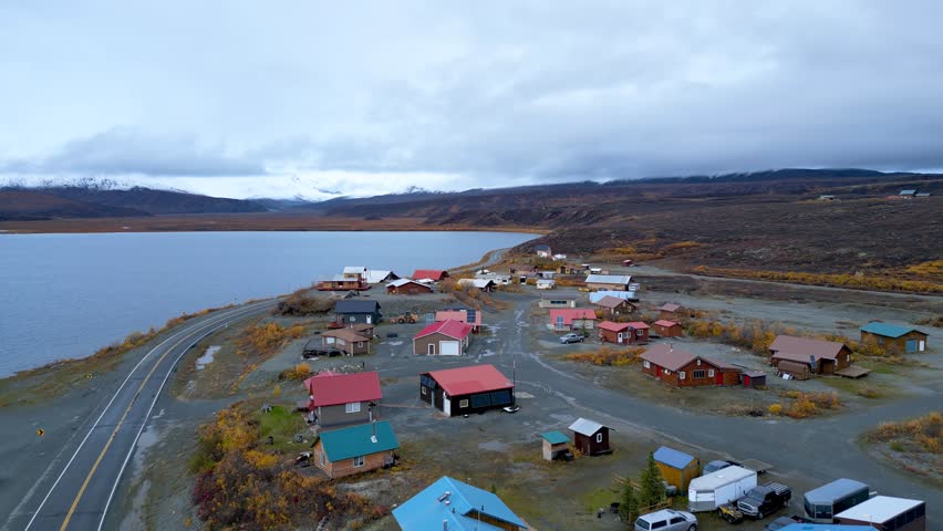 Aerial view of a remote Alaskan village nestled along a lake with  with colorful homes on a cloudy day.
