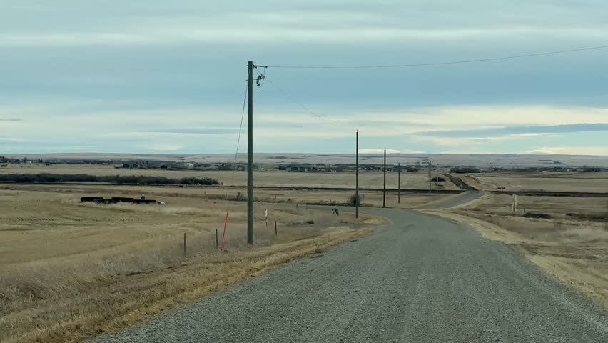 Driver POV on rural gravel road through Alberta prairie under dramatic cloudy sky
