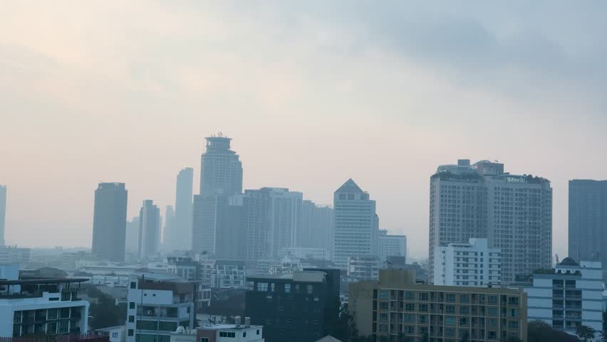 Wide static shot of skyscrapers in Bangkok obscured by heavy smog under a grey sky