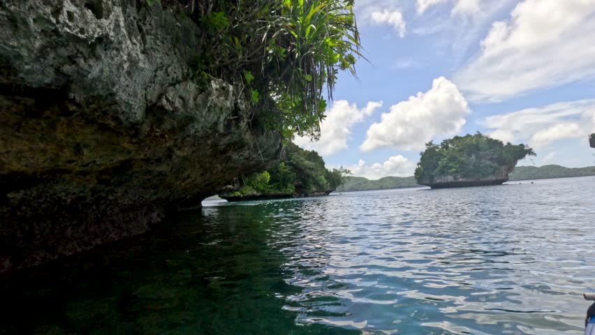 A first-person perspective camera glides past jagged limestone cliffs over clear turquoise tropical water
