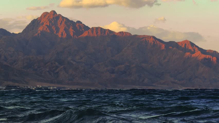 Last sun rays on the top of mountain and sea waves in foreground