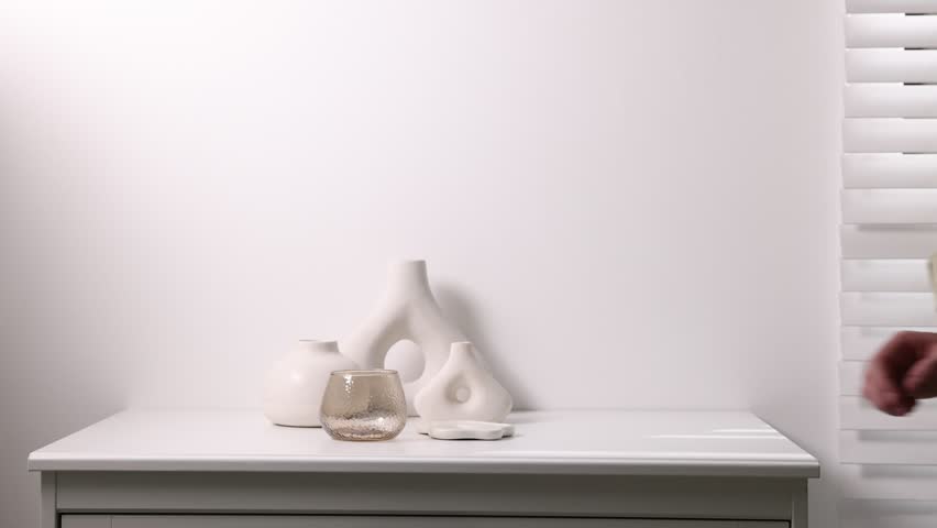 Man putting candle holder and vase onto cabinet near white wall indoors, closeup