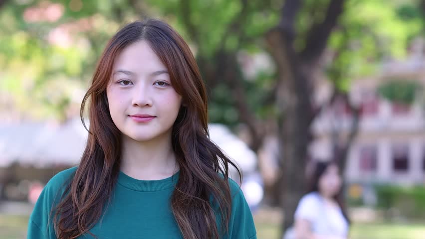 A close-up shot of a cheerful Asian woman smiling in a sunny outdoor park.