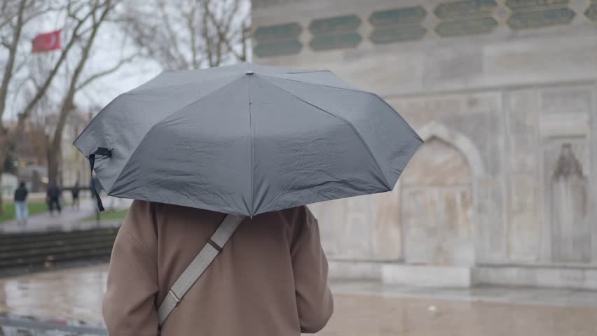 Person with umbrella walking in rain on city street cinematic footage