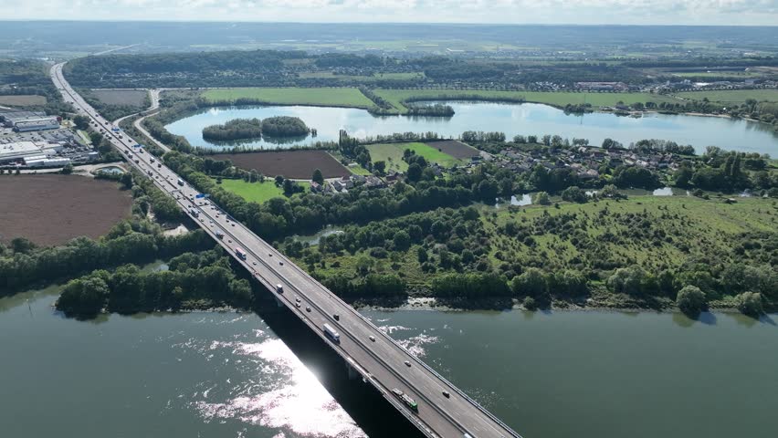 Aerial tilt-down to a top-down view of a highway bridge spanning a river in rural France, showcasing moving vehicles and lush greenery.