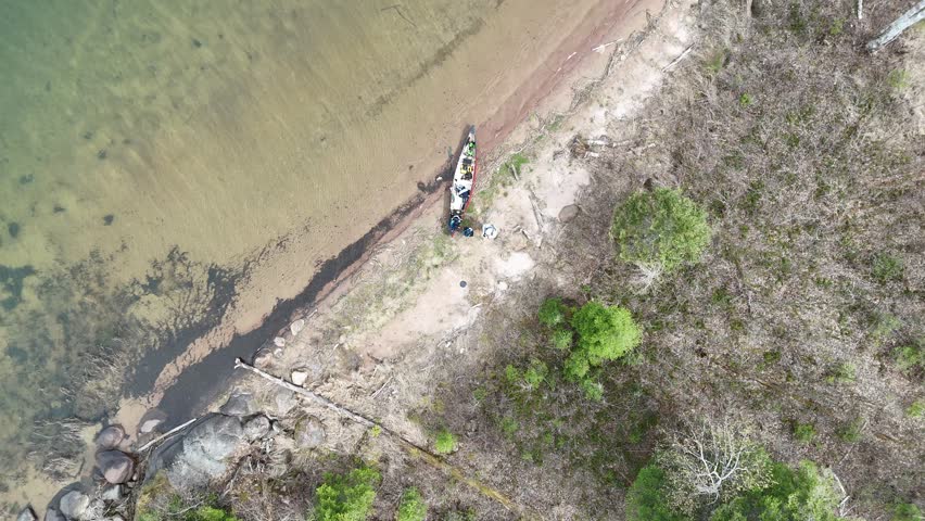Canoe on a sandy beach beside a lake in Whiteshell Provincial Park Manitoba. Aerial view looks down and slowly rises revealing shoreline, boreal forest and clear lake water.