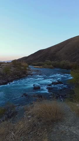 Panoramic view of a turbulent mountain river, evening, twilight, early autumn, blue water rushing down from the mountains in a powerful stream, vertical video