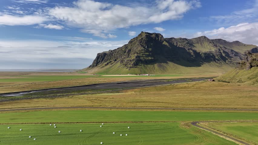 Eyjafjöll, Iceland - Green Farmland Stretches Across the Plains Beneath a Rugged Mountain - Aerial Drone Shot