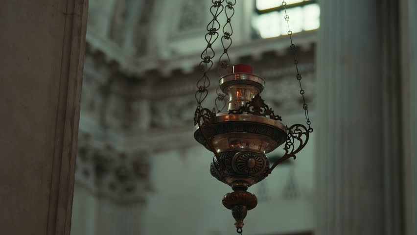 Antique bronze sanctuary lamp with candle flame hanging in Cattedrale di Santa Maria Assunta, Brescia, Italy, slow pan