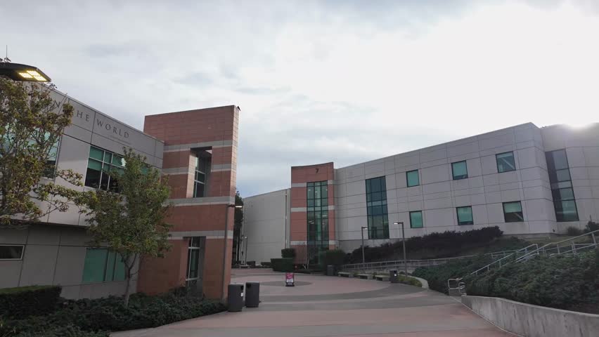 Point-of-view perspective walking tour through the empty campus of Skyline College in San Bruno, California, showcasing its modern architecture and paved pathways on a cloudy day