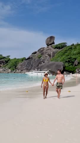 Sunshine illuminates the serene shores of Similan Islands as a couple walks hand in hand along the soft, white sand. Clear blue waters and stunning rock formations create a perfect vacation backdrop.