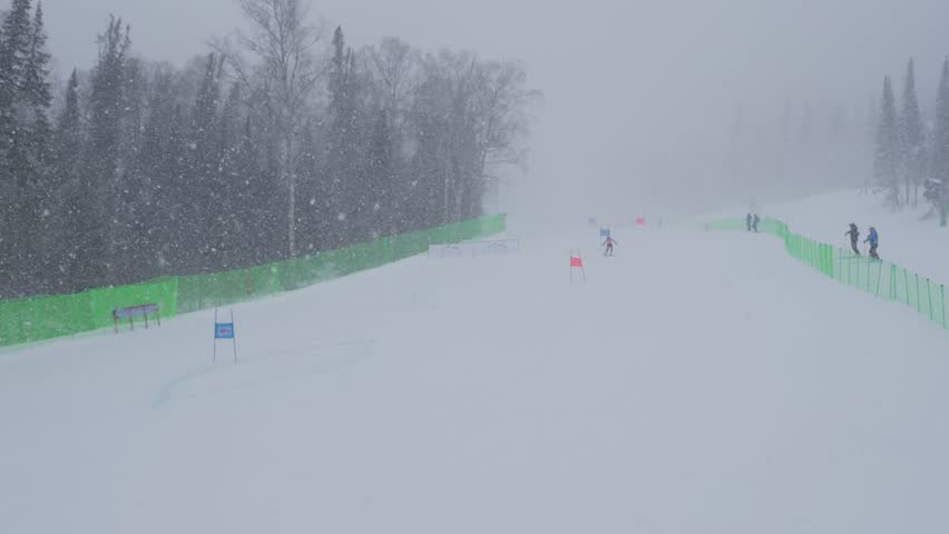 Skier Speeds Downhill. Skier Swiftly Descending Through Snowcovered Gates And Safety Barriers. Highspeed Skier Cuts Through Snowy Slalom Course With Flags And Protective Netting In View
