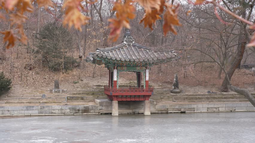 Slow motion landscape view of ancient temple hut resting upon frozen lake with forest woodlands in the background Secret Garden courtyard at Changdeokgung Palace Seoul city South Korea travel nature