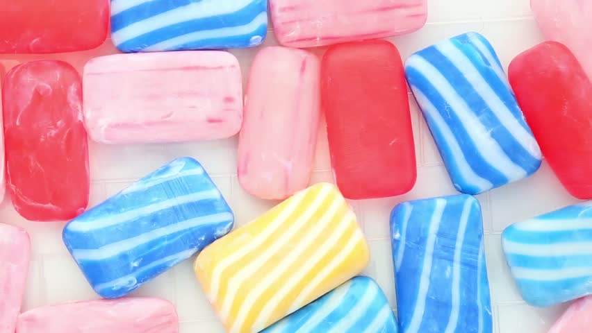 Water is poured onto colored soaps. Hands squeeze bars of soap into the water's growing foam as the pink and blue bars disappear under the thick white foam, creating a soothing ASMR