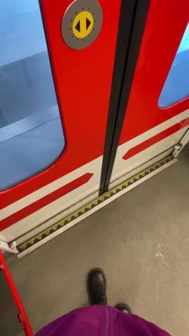 Boarding red train with boot at threshold above yellow warning line, platform tactile paving and grey tiles visible, commuter stepping into carriage. POV first person view