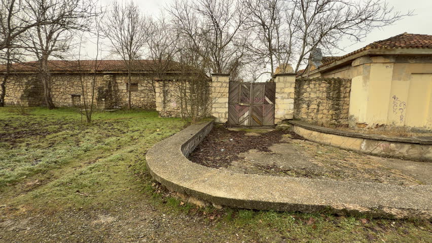 An old stone structure with wooden doors sits along a dirt trail. Bare winter trees and frost-covered grass create a lonely, haunting atmosphere. The scene feels still and full of history.