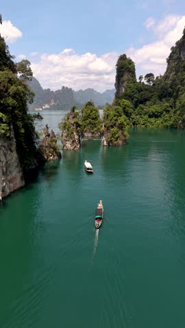 Experience the breathtaking beauty of Khao Sok National Park as a traditional boat glides through tranquil emerald waters, surrounded by lush forests and limestone cliffs in Thailand