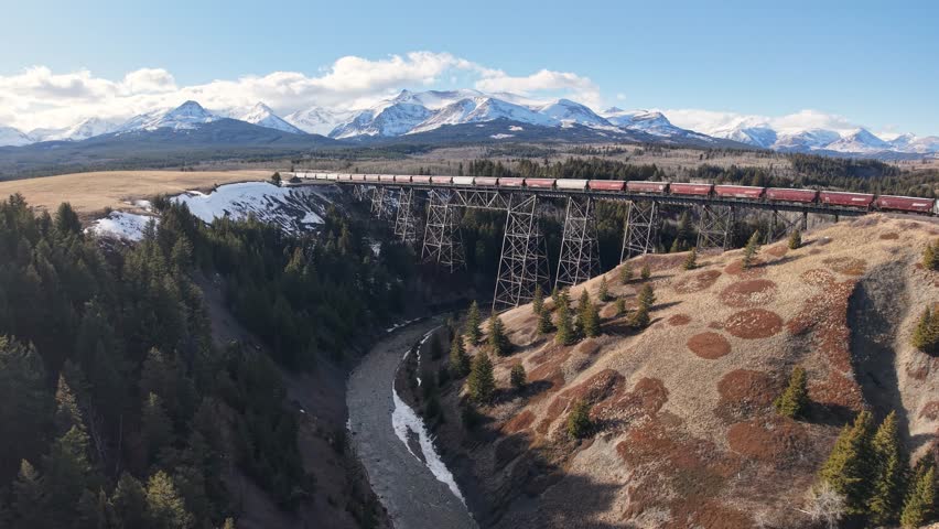 Aerial panorama of a winding river with evergreen forest and distant snow-capped mountains near Whitefish, Montana.